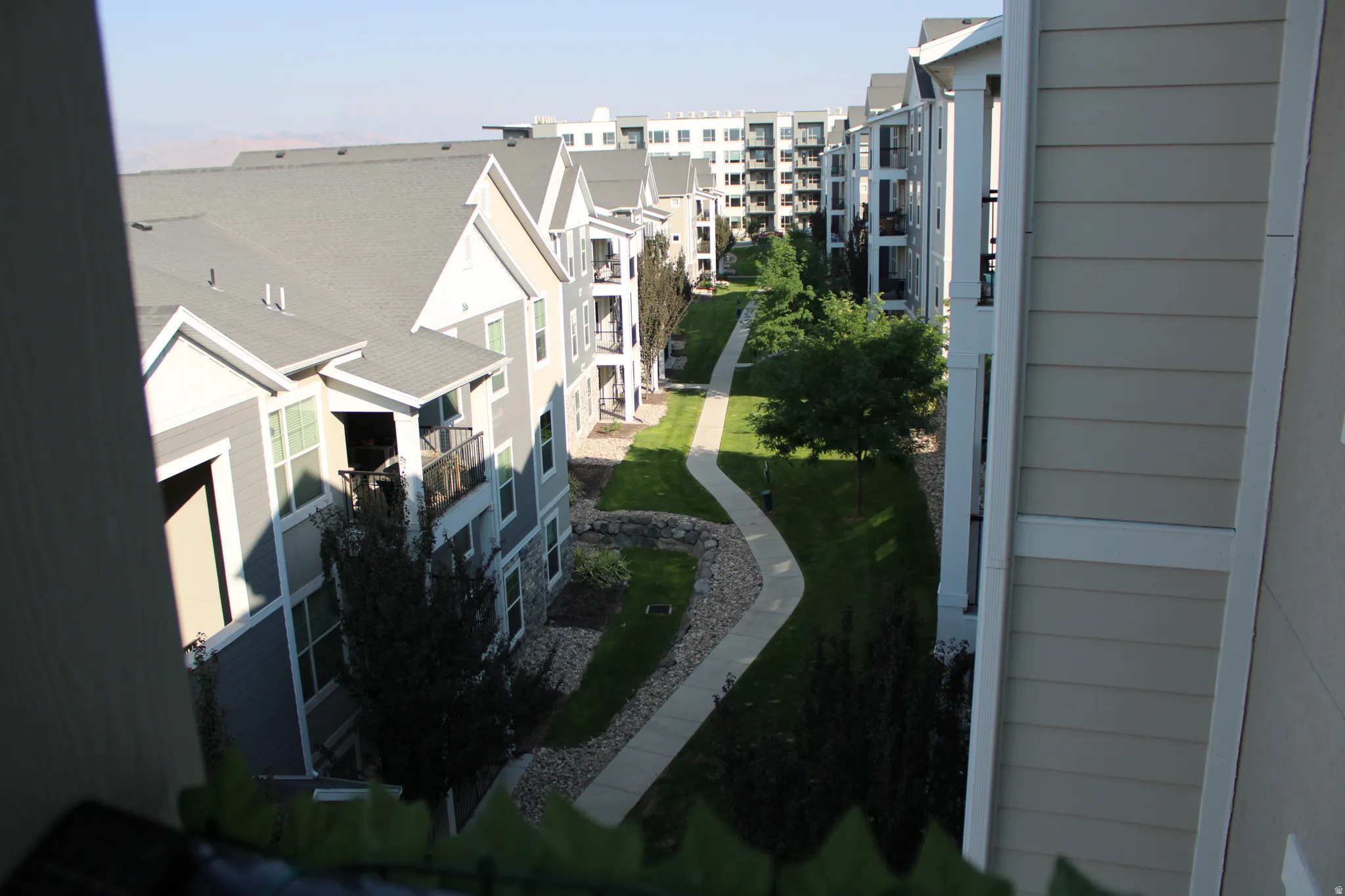 Multiple residential structures with balconies and a central landscaped courtyard featuring a meandering paved pathway