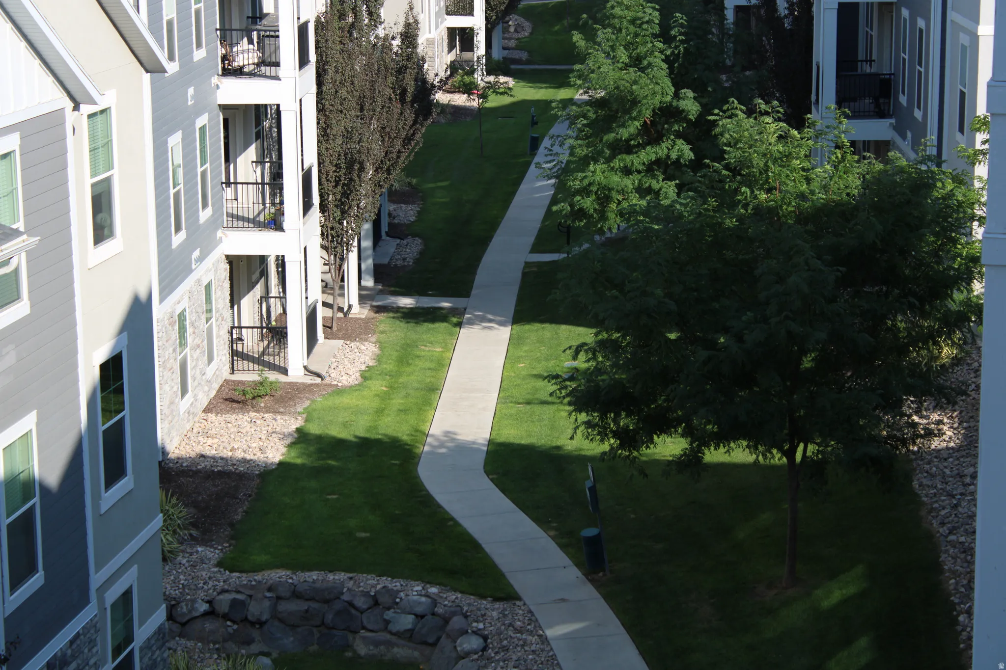 Manicured green space with a winding paved pathway, surrounded by mature trees and stone landscaping