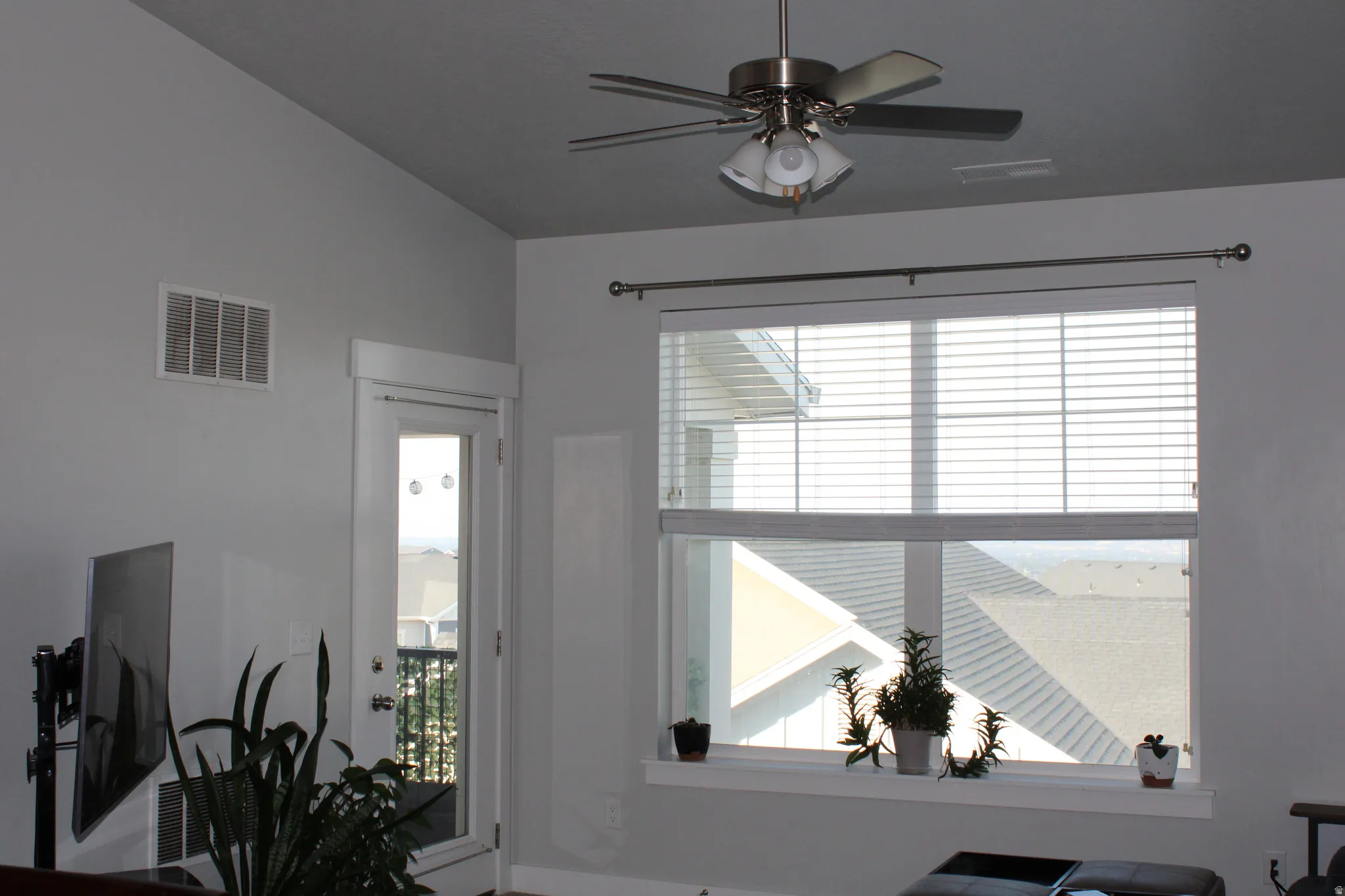 Vaulted ceiling, ceiling fan with integrated lighting, glass-paneled door, large window with blinds, and white trim throughout