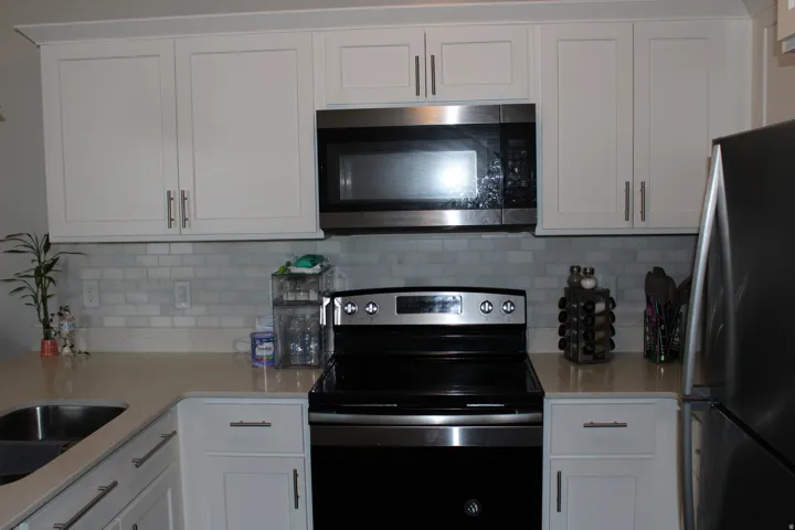 White shaker-style cabinetry, stainless steel appliances, light-toned countertops, and subway tile backsplash
