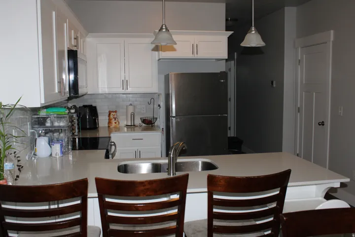 Kitchen featuring white shaker cabinetry, stainless steel sink, light-toned countertop, and tile backsplash