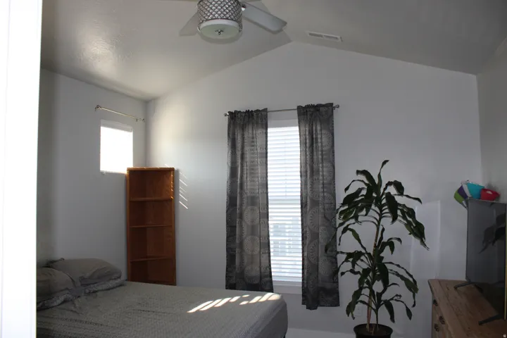 Vaulted ceiling with a ceiling fan, two windows, and white walls