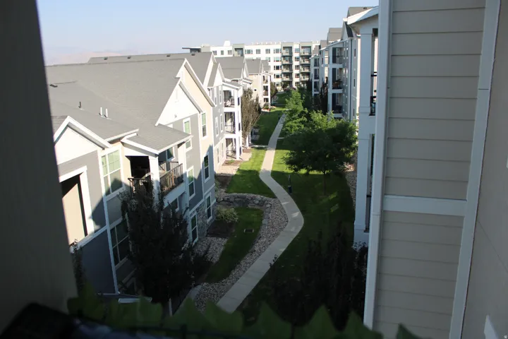 Multiple residential structures with balconies and a central landscaped courtyard featuring a meandering paved pathway
