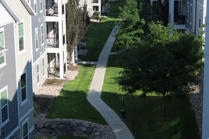 Manicured green space with a winding paved pathway, surrounded by mature trees and stone landscaping