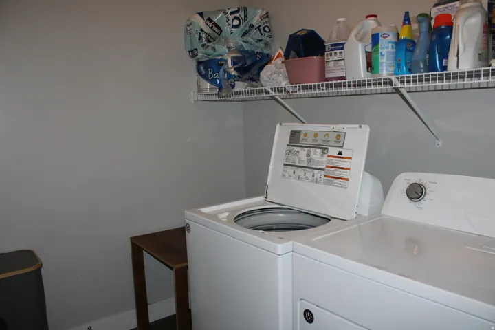 Laundry area with white appliances and an overhead wire shelf