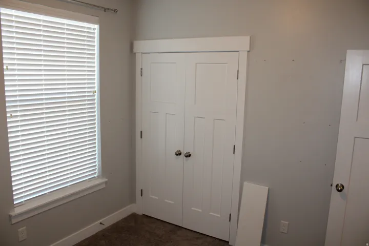 White panel doors, window with horizontal blinds, neutral wall paint, and carpeted flooring