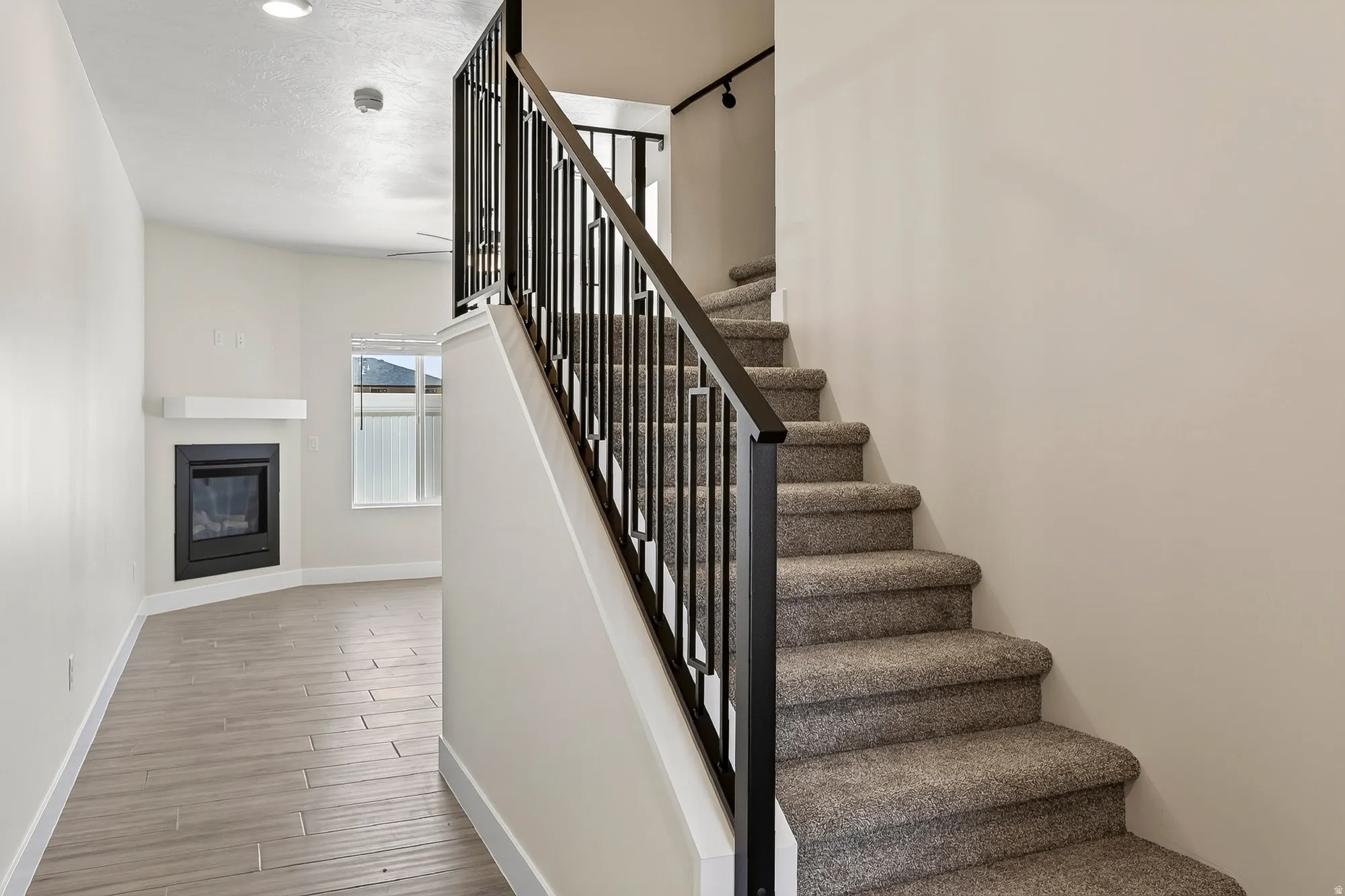 Integrated carpeted staircase with a black metal railing, wood-finish flooring, and a corner fireplace with a white mantel