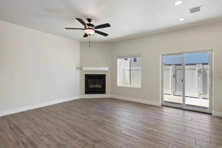 Wood-finish flooring throughout, featuring a corner fireplace with a white mantel, and a ceiling fan with integrated lighting