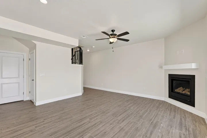 Spacious room featuring wood-finish tile flooring, a corner fireplace with a white mantel, and a ceiling fan with integrated lighting