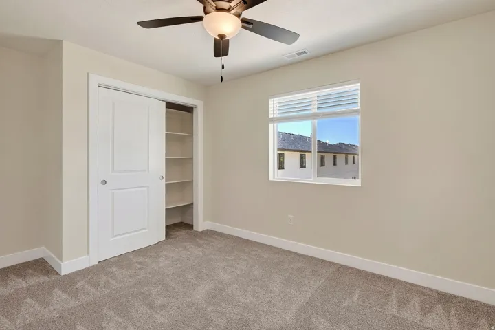 Neutral-toned walls, plush carpeting, and a ceiling fan with integrated lighting