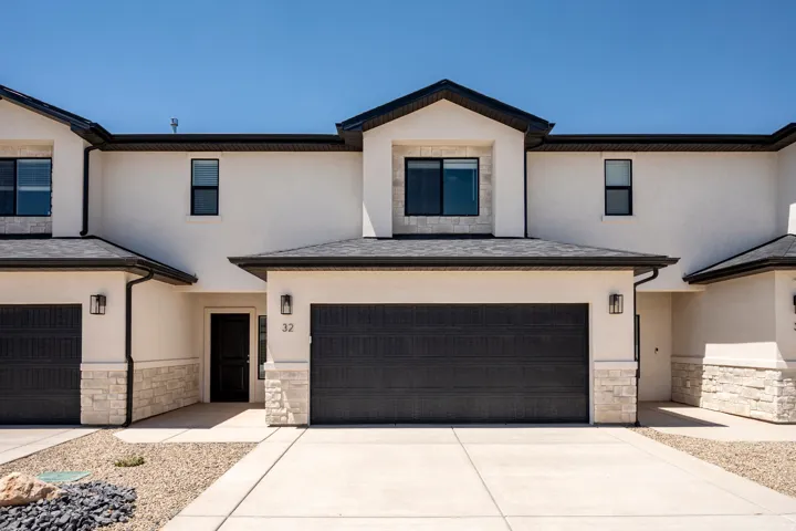 Modern stucco exterior with stacked stone accents, a dark asphalt shingle roof, and black frame windows