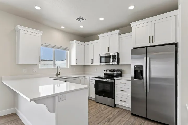 White shaker cabinetry, stainless steel appliances, light-colored countertops, wood-finish flooring, and recessed lighting