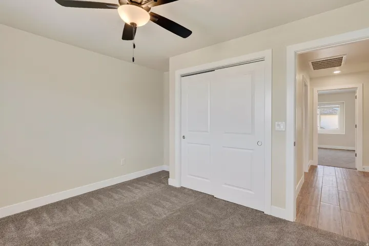 Ceiling fan with integrated lighting, carpeted flooring, sliding closet doors, wood-look tile flooring in the hallway