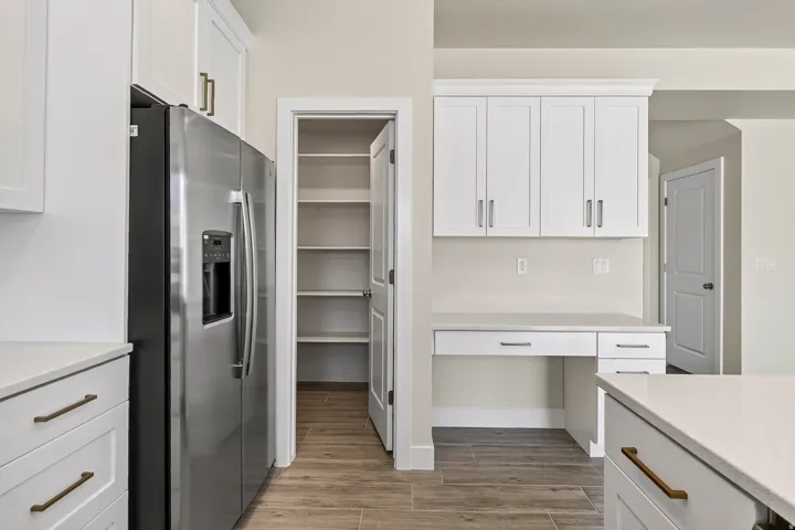 Kitchen featuring stainless steel refrigerator, white cabinetry with bronze hardware, light countertops, wood-finish flooring, and a built-in desk area