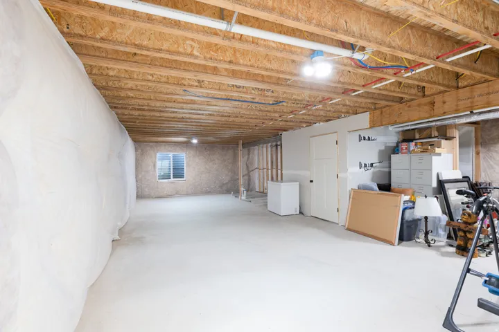 Unfinished basement with exposed wood joists, concrete flooring, and a white framed window