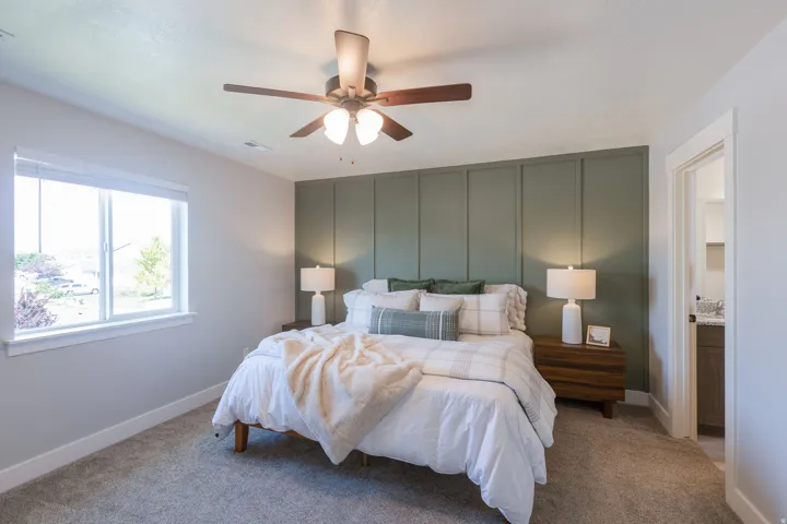 Textured accent wall, ceiling fan with light fixture, double-pane window, carpeted flooring, and built-in door frame