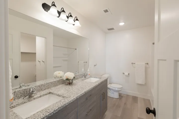Dual vanity with light-toned countertop, integrated sinks, and contemporary wall-mounted lighting