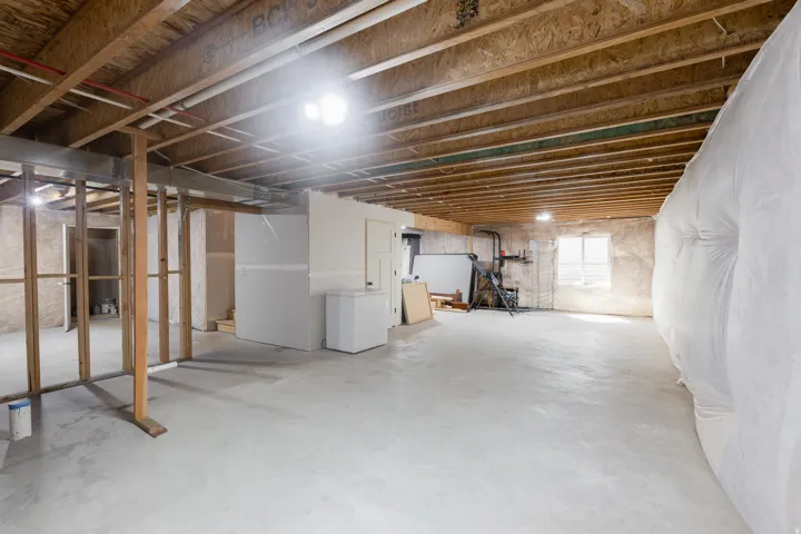 Exposed wood ceiling joists and subfloor, concrete flooring, partial framing, and a window