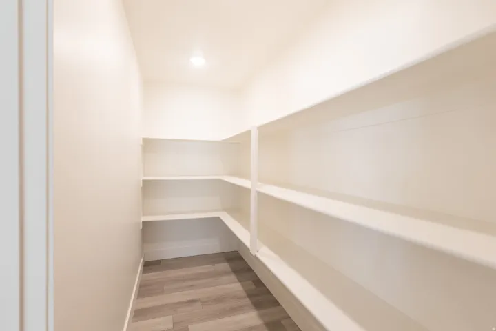 Walk-in pantry featuring built-in shelving, wood-finish flooring, recessed lighting, and light-toned walls