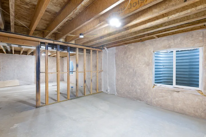 Daylight basement featuring exposed ceiling joists, concrete flooring, wall insulation, a window, and wood framing