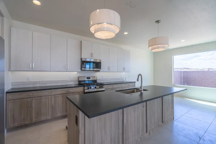 Modern kitchen featuring a large central island with a stainless steel sink, dark countertops, and two-tone cabinetry