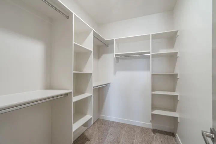 Walk-in closet featuring built-in white shelving, multiple hanging rods, and carpet flooring