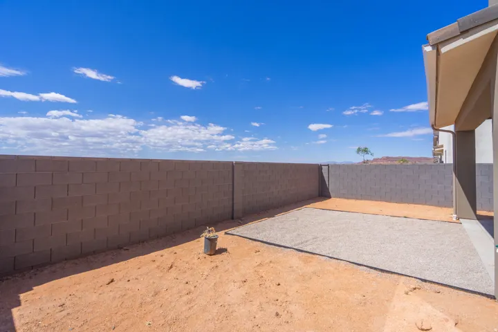 Rear yard featuring a full-height block fence, an extended covered patio, and a gravel-covered entertainment area