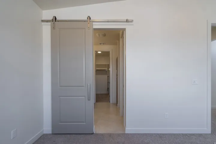 Gray barn door with brushed steel hardware, opening to a hallway with tile flooring