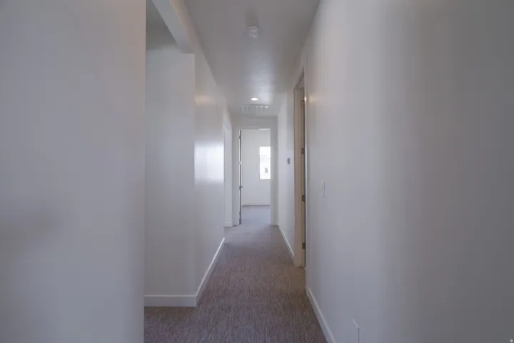 Hallway with light gray carpet, white baseboards, white walls, and recessed lighting