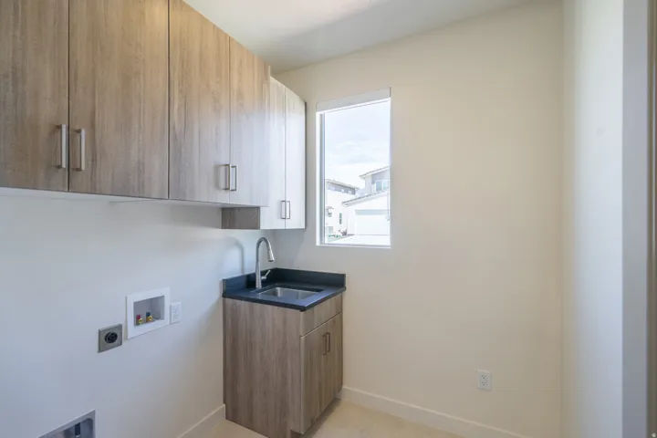 Laundry room featuring extensive wood-finish cabinetry, a utility sink with a gooseneck faucet, a dark countertop, and a window