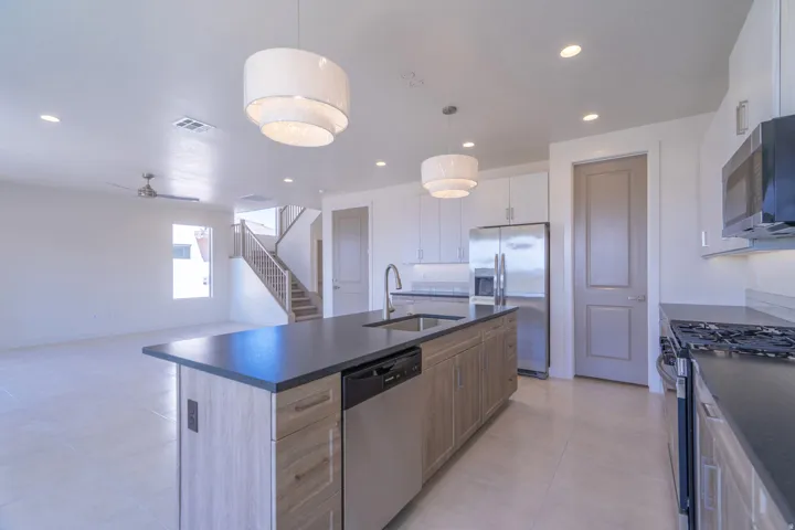 Open-concept kitchen featuring a large island with dark countertops, stainless steel appliances, and wood-finish cabinetry