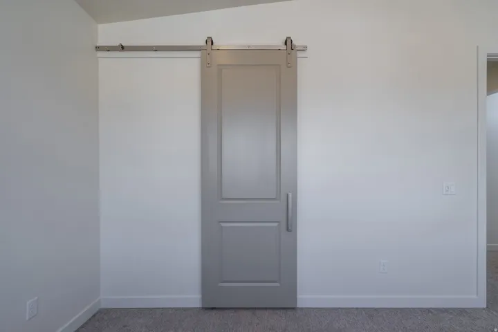 Modern barn door with a horizontal pull handle, finished in a soft gray, set against white walls and light gray carpet flooring