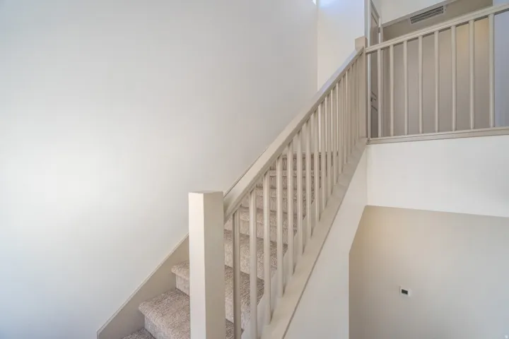 Staircase with carpeted treads and painted wood balusters, featuring a neutral color palette