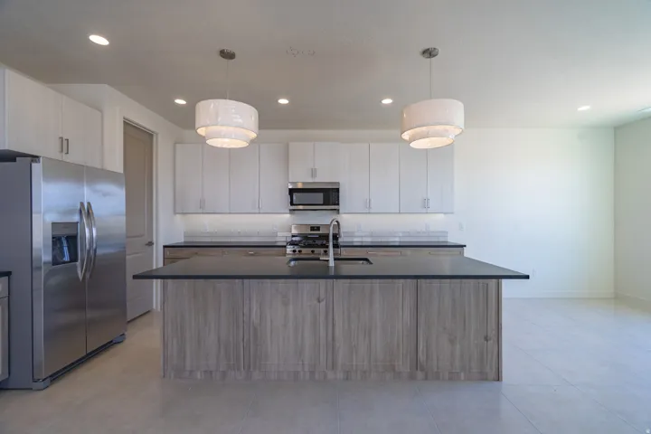 Modern kitchen featuring a central island with a sink, stainless steel appliances, light wood-finish cabinetry, and recessed lighting