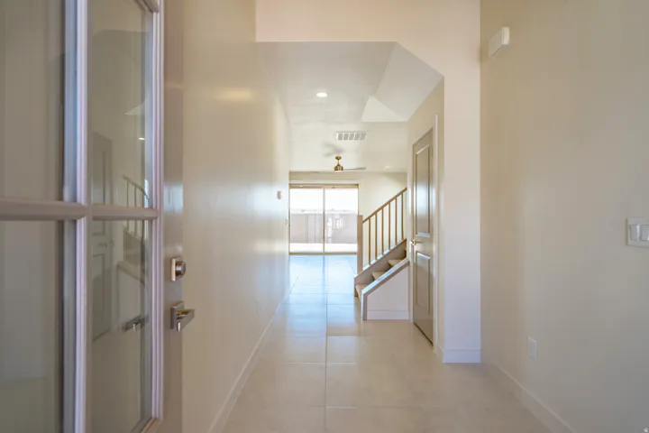 Entryway featuring a partially glass-paneled door, light tile flooring, an angled ceiling, and a wooden staircase with a railing