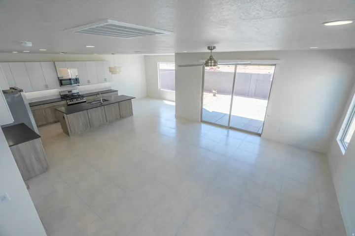 Open-concept interior featuring light-toned tile flooring, a contemporary kitchen with wood-finish cabinetry and dark countertops, stainless steel appliances, and a central island with an undermount sink