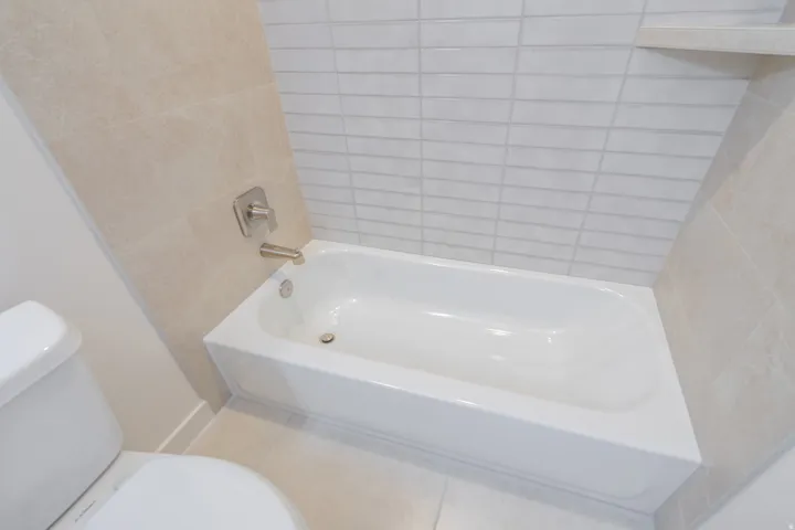 White drop-in bathtub with brushed nickel fixtures, surrounded by light-toned rectangular tile