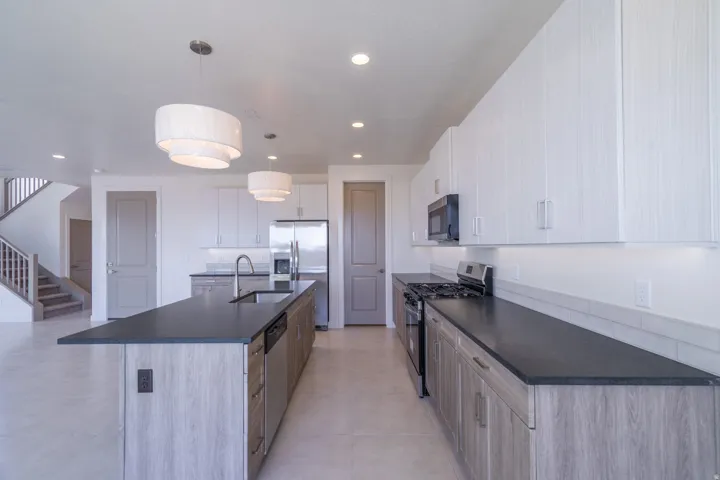 Contemporary kitchen featuring a large island with an integrated sink, stainless steel appliances, two-tone cabinetry, and sleek pendant lighting