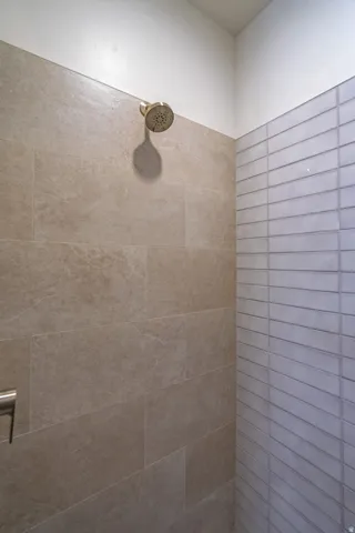 Shower enclosure featuring a bronze-finish showerhead, large-format beige wall tiles, and horizontal white textured accent tiles