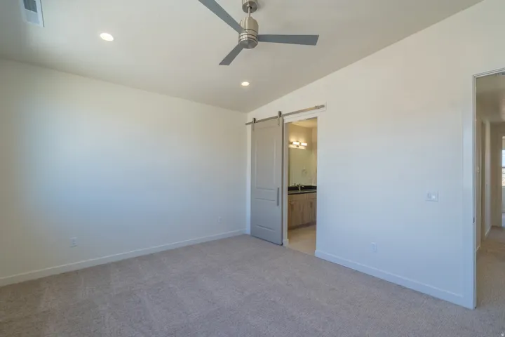 Carpeted room featuring a modern ceiling fan, recessed lighting, and a barn door leading to an en-suite bathroom