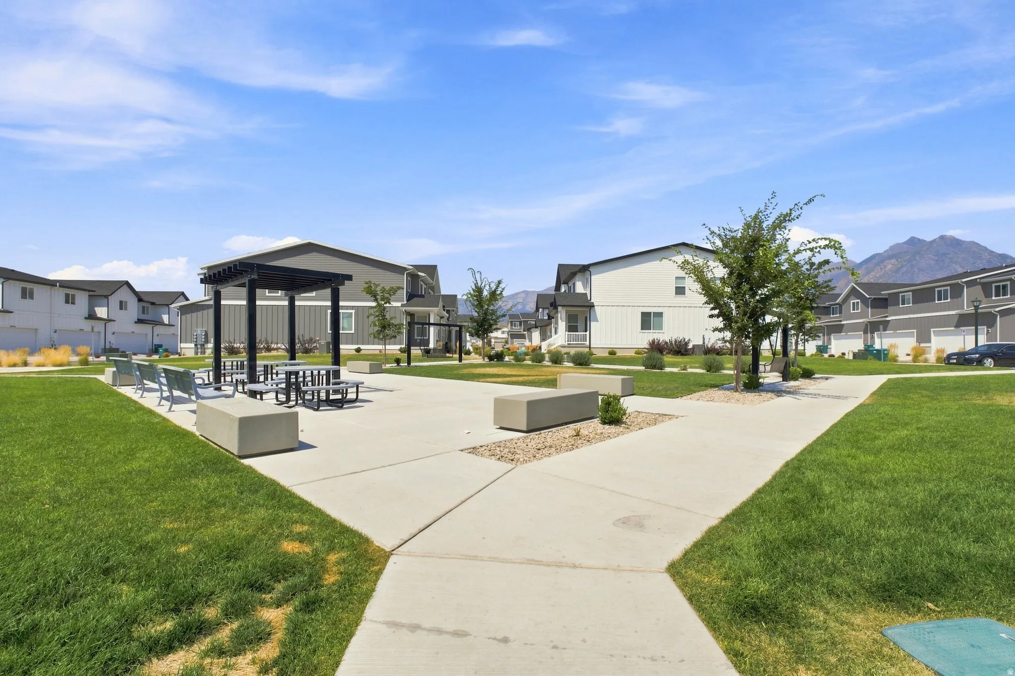 Expansive green spaces featuring a concrete pathway, a shaded pergola, and concrete seating areas
