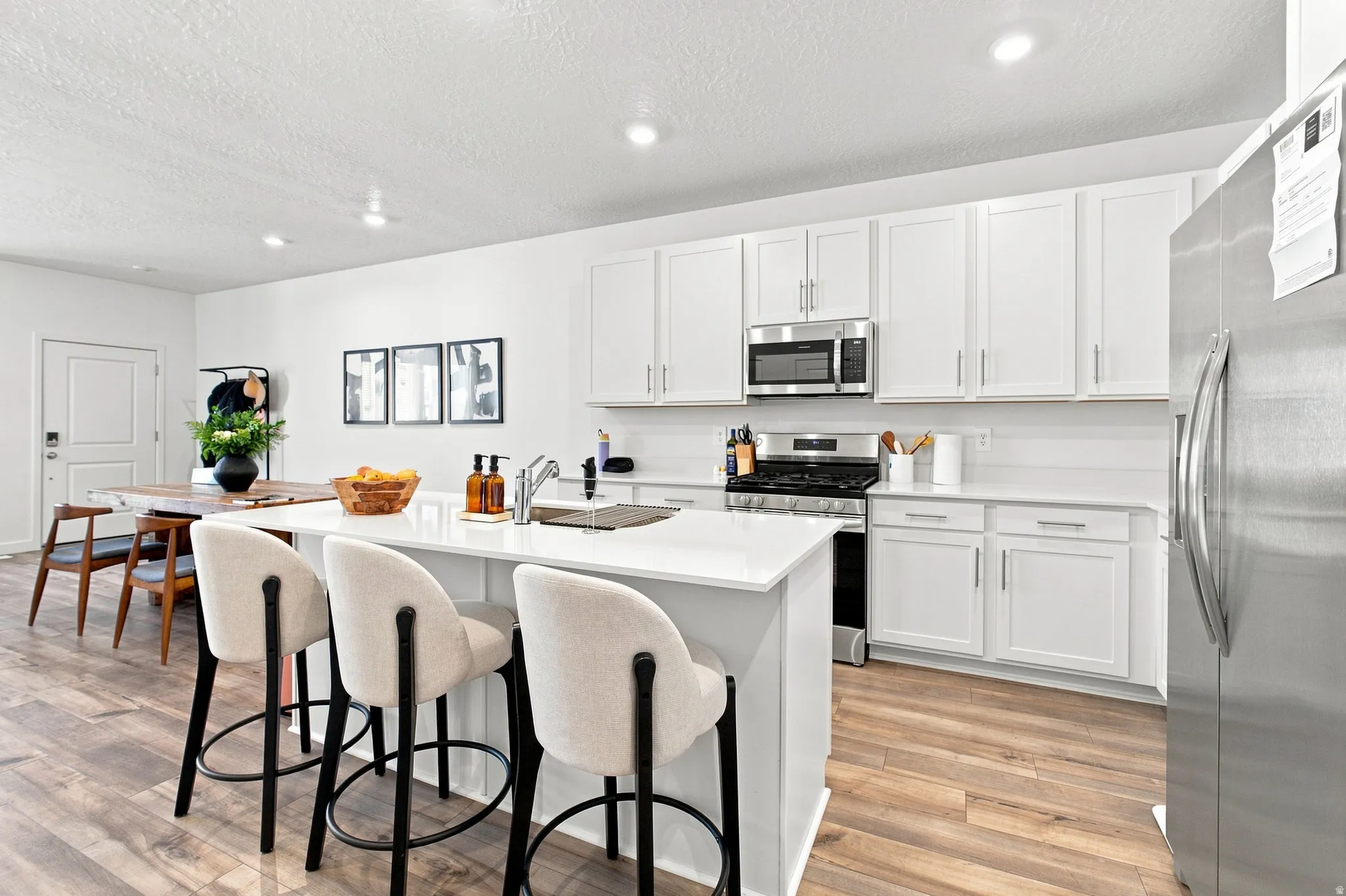 Kitchen featuring white cabinetry, stainless steel appliances, an island with an integrated sink, white countertops, and wood-finish flooring