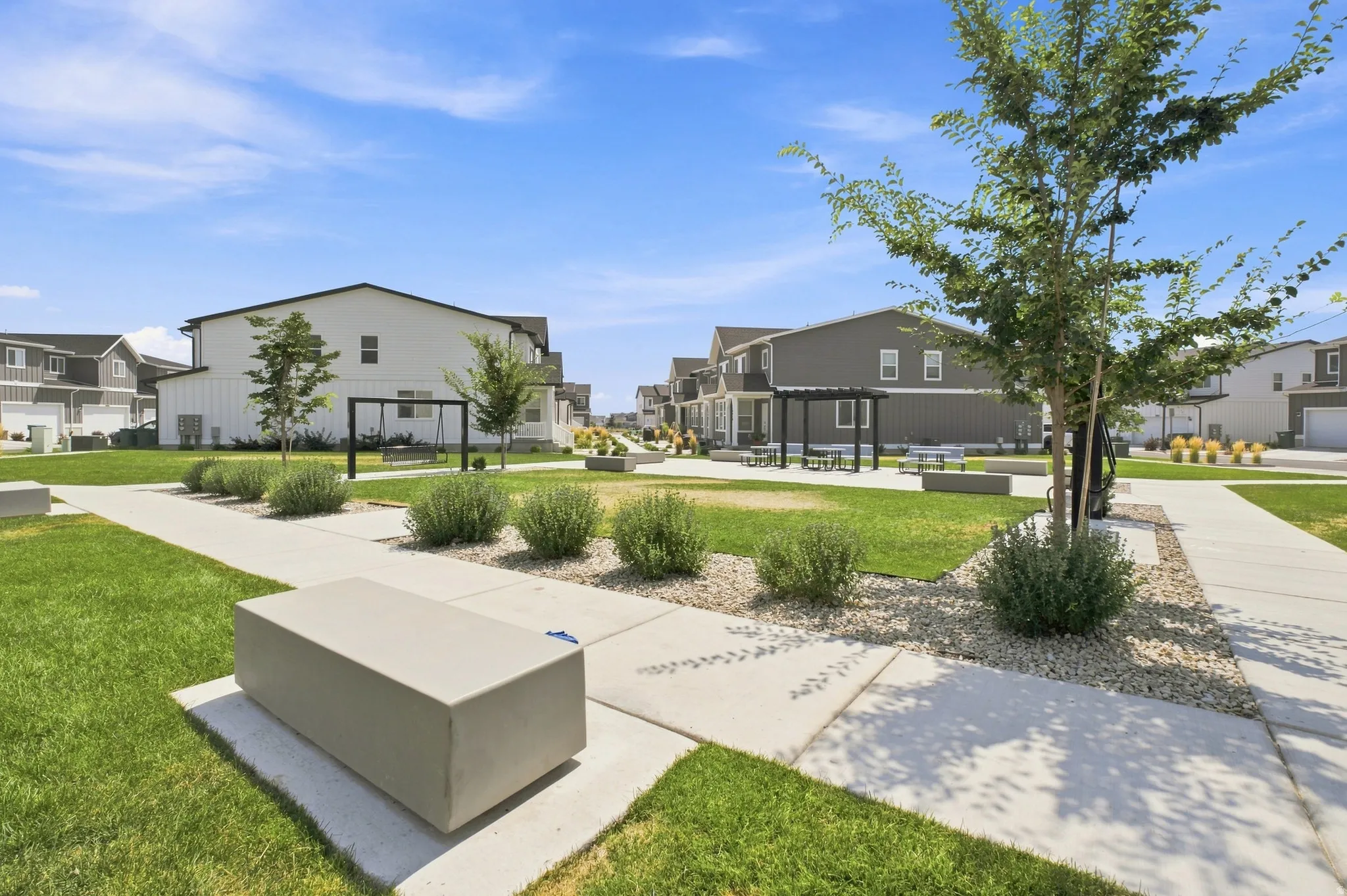 Community green space featuring concrete pathways, manicured lawns, and integrated concrete benches