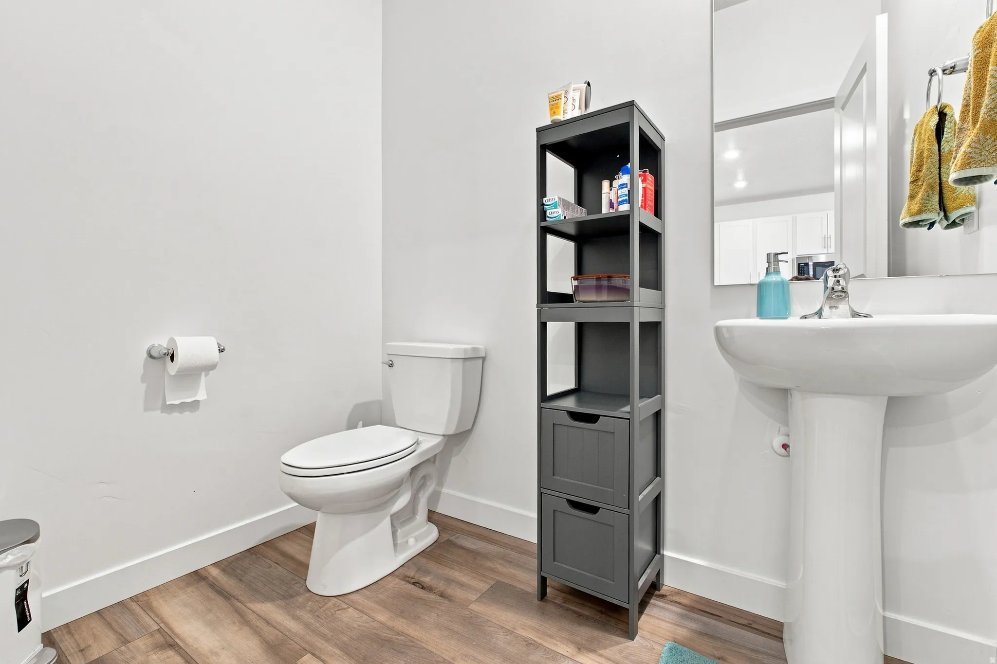 Pedestal sink with chrome faucet, toilet, wood-finish flooring, and a framed wall mirror