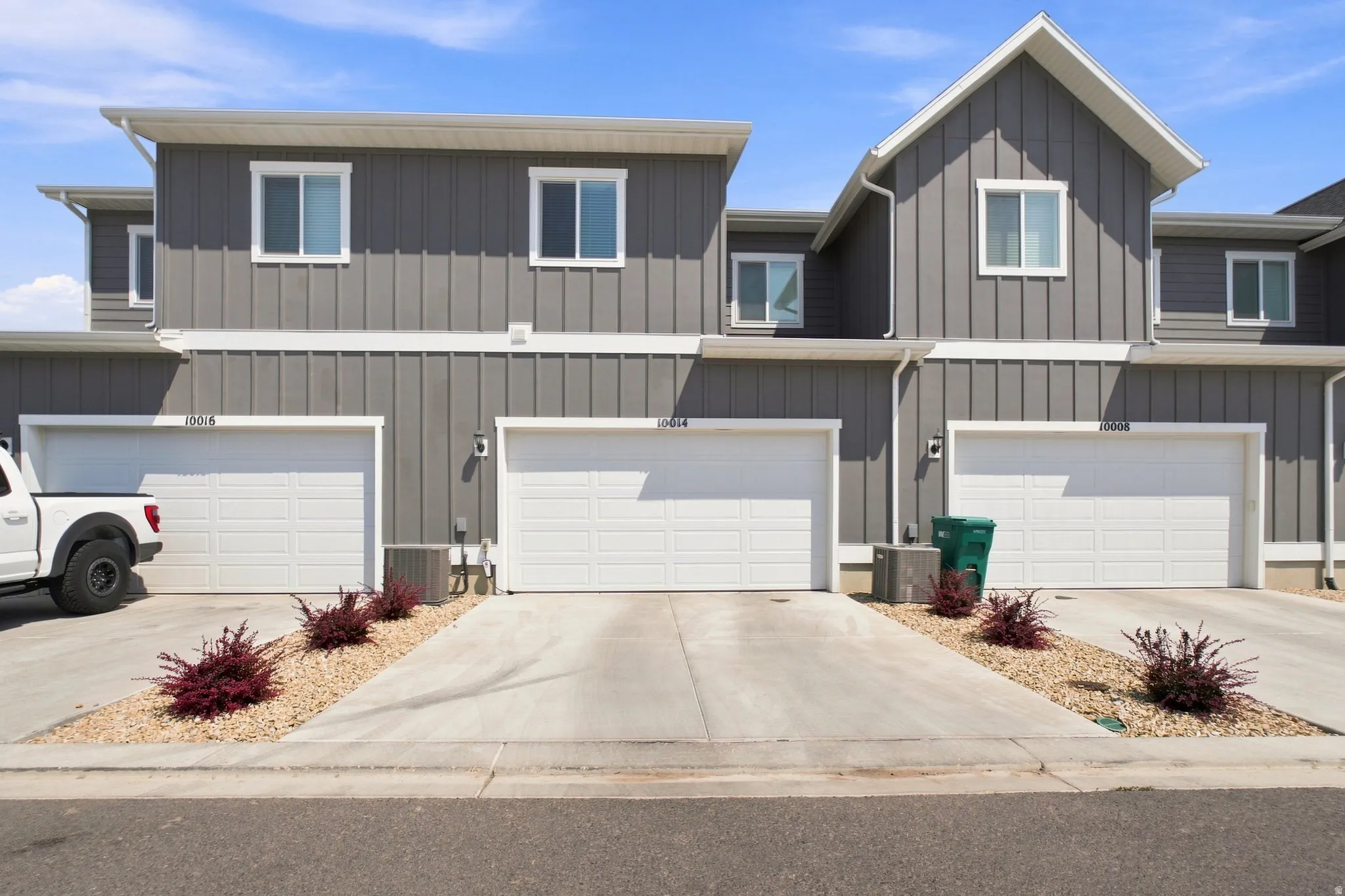 Vertical siding exterior with white trim, multiple windows, and individual garage doors