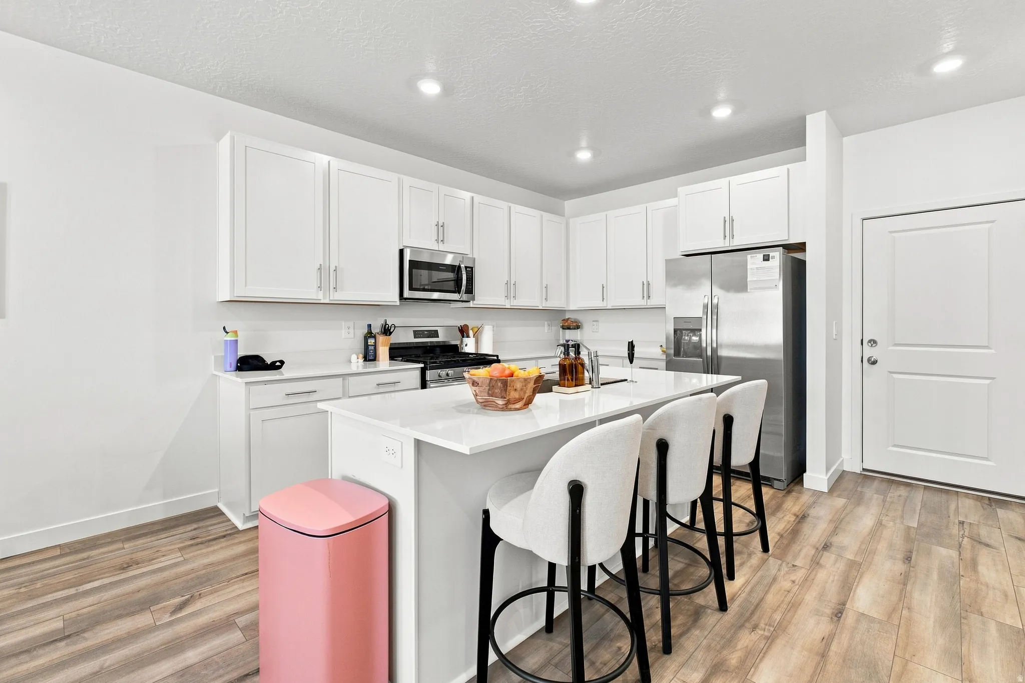 White cabinetry, stainless steel appliances, white countertops, wood-finish flooring, and recessed lighting
