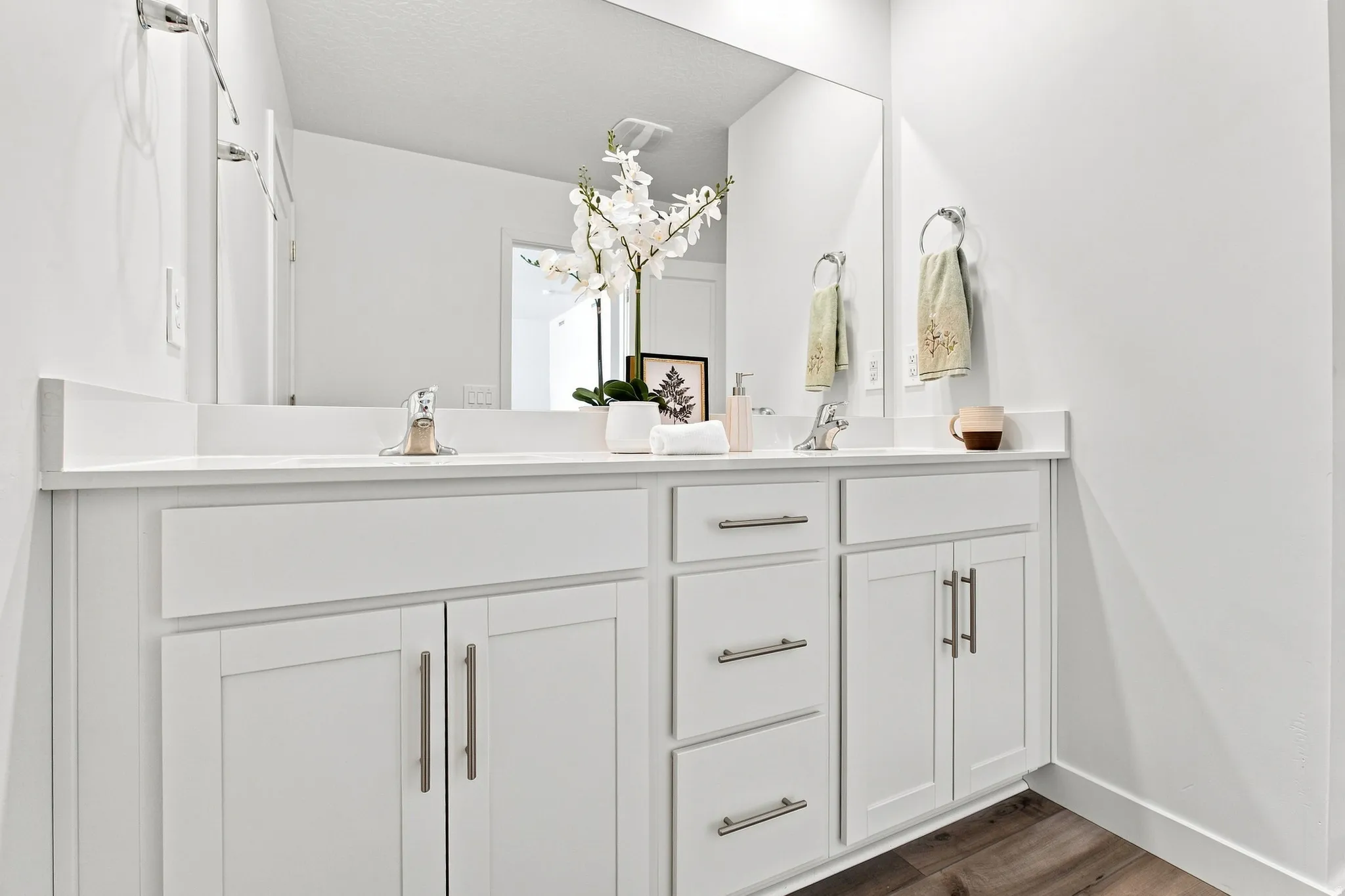 Dual vanity with white cabinetry and brushed nickel hardware, integrated sinks, white countertops, and wood-finish flooring
