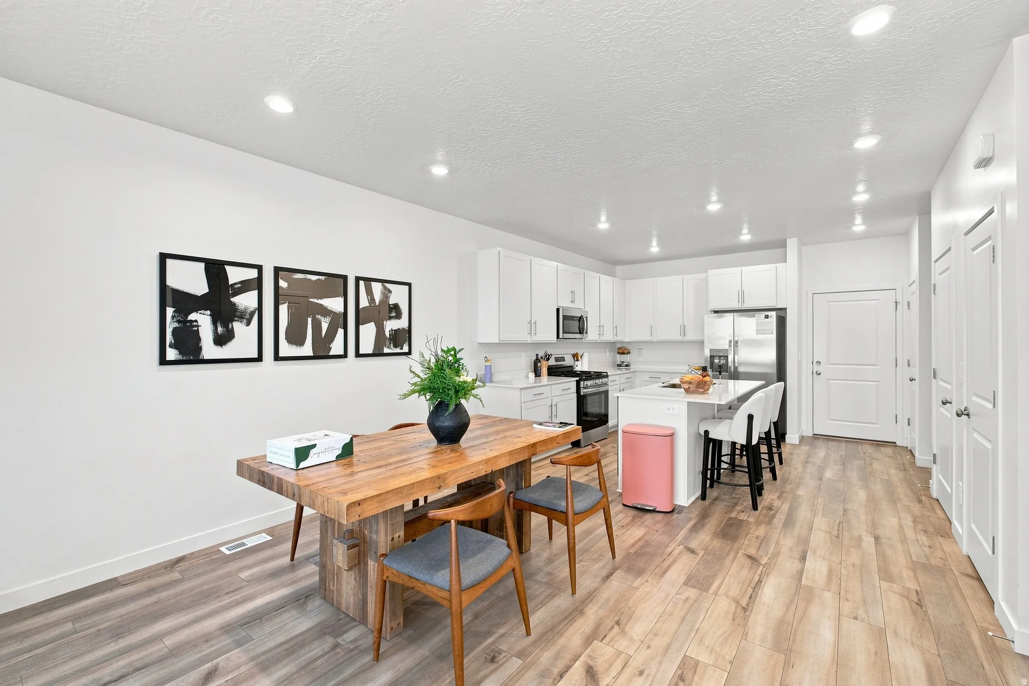 Open-concept living space featuring wood-finish flooring, recessed lighting, white cabinetry, a kitchen island with seating, and stainless steel appliances