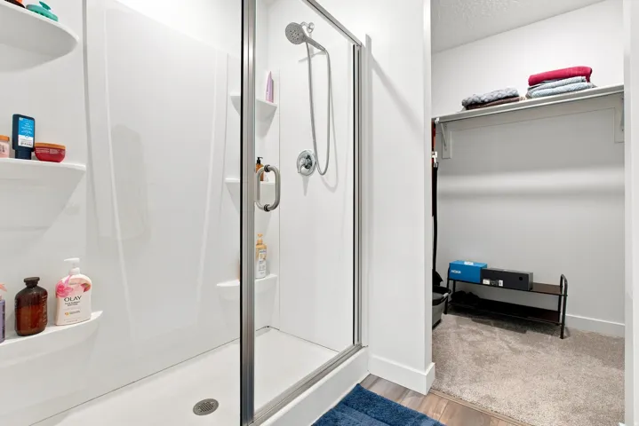 Shower with clear glass enclosure, overhead shower fixture, and integrated shelving