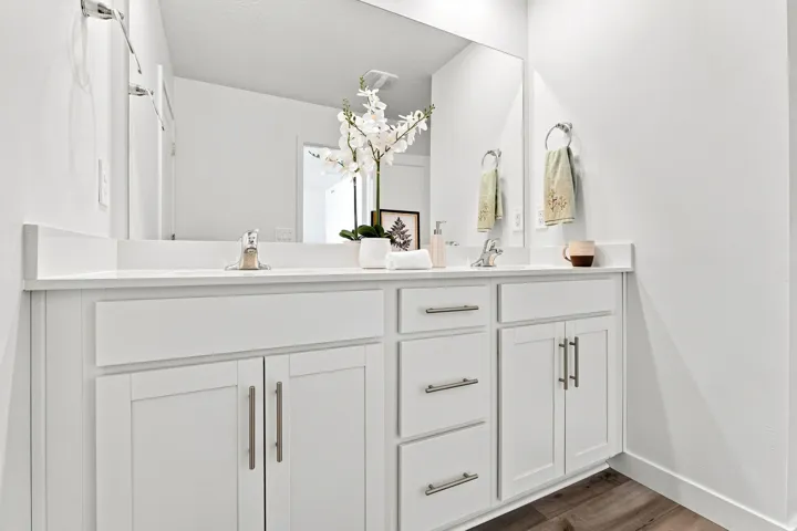 Dual vanity with white cabinetry and brushed nickel hardware, integrated sinks, white countertops, and wood-finish flooring